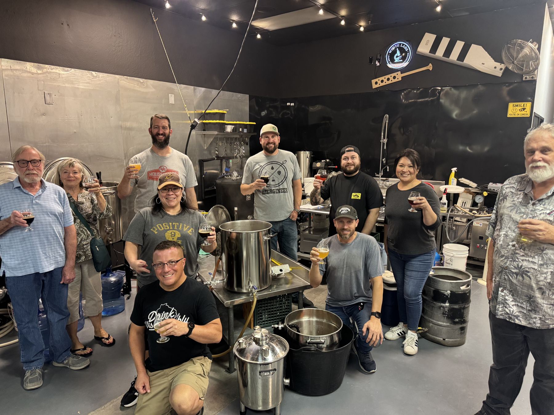 A brewing class raising their glasses around the brew system at What Ale's Ya